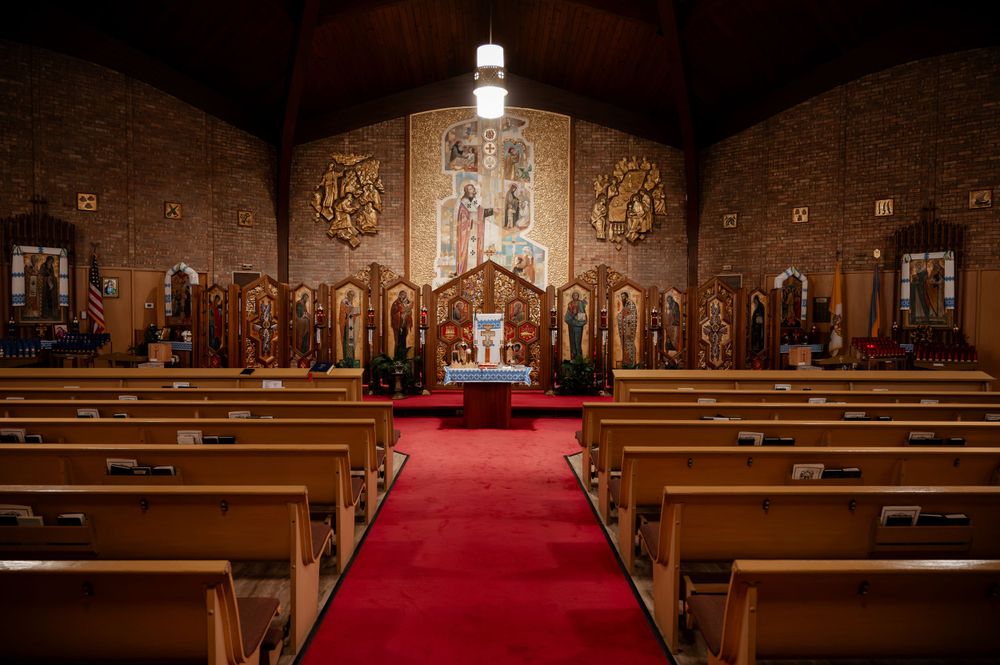 Empty Orthodox church interior with red carpet aisle, wooden pews, and ornate golden iconostasis.