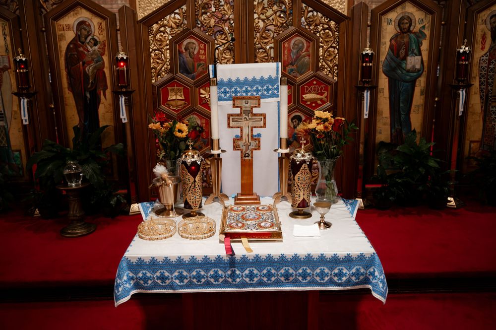 Orthodox church altar with decorative cross, floral arrangements, and religious icons on display.