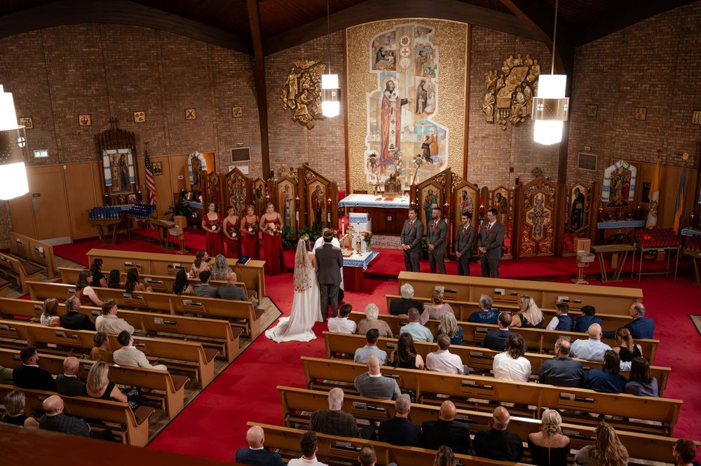 Wedding ceremony in Orthodox church with bridal party at altar and guests seated in wooden pews.