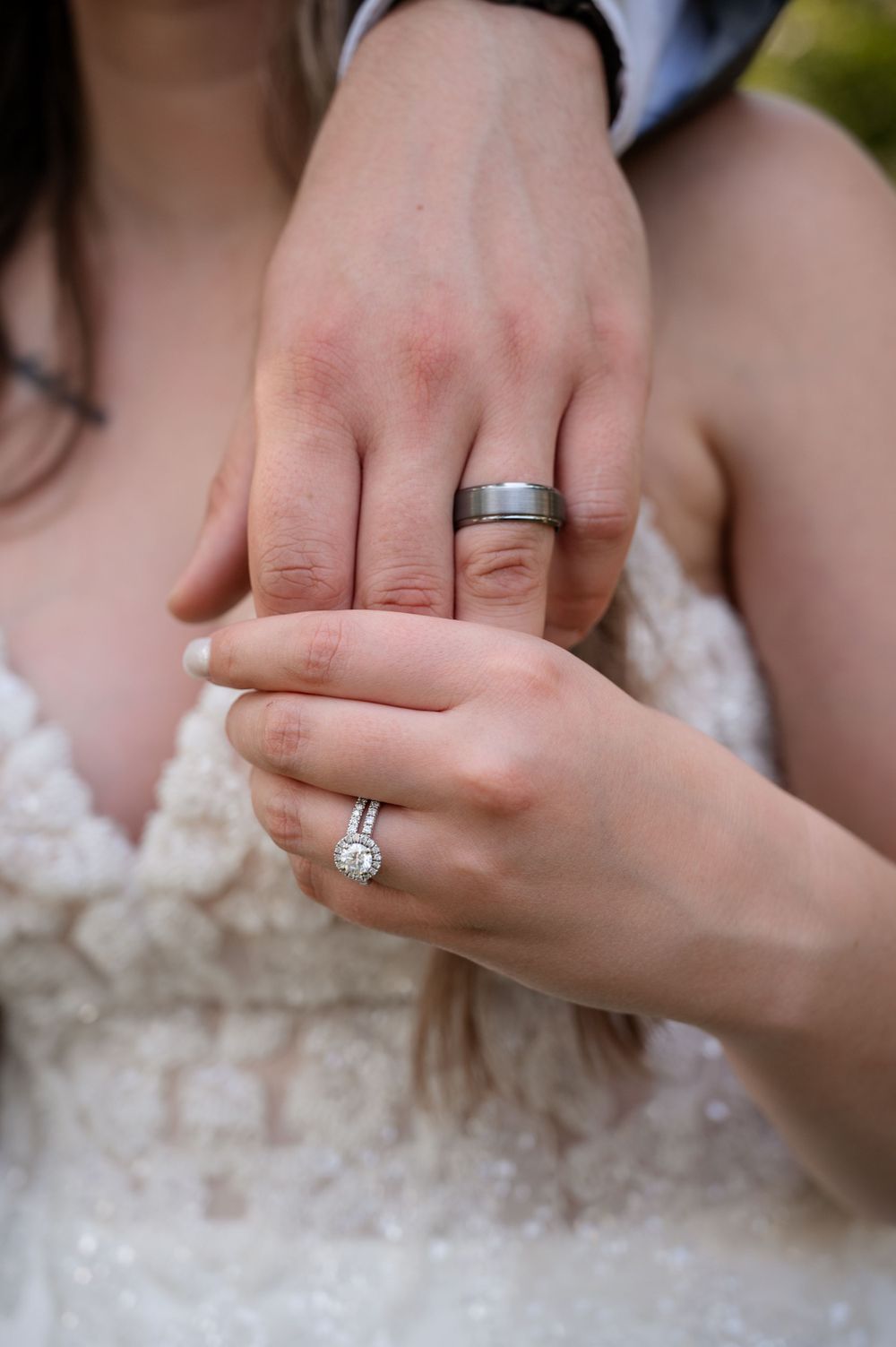 Close-up of bride and groom hands showing diamond engagement ring and tungsten wedding band.