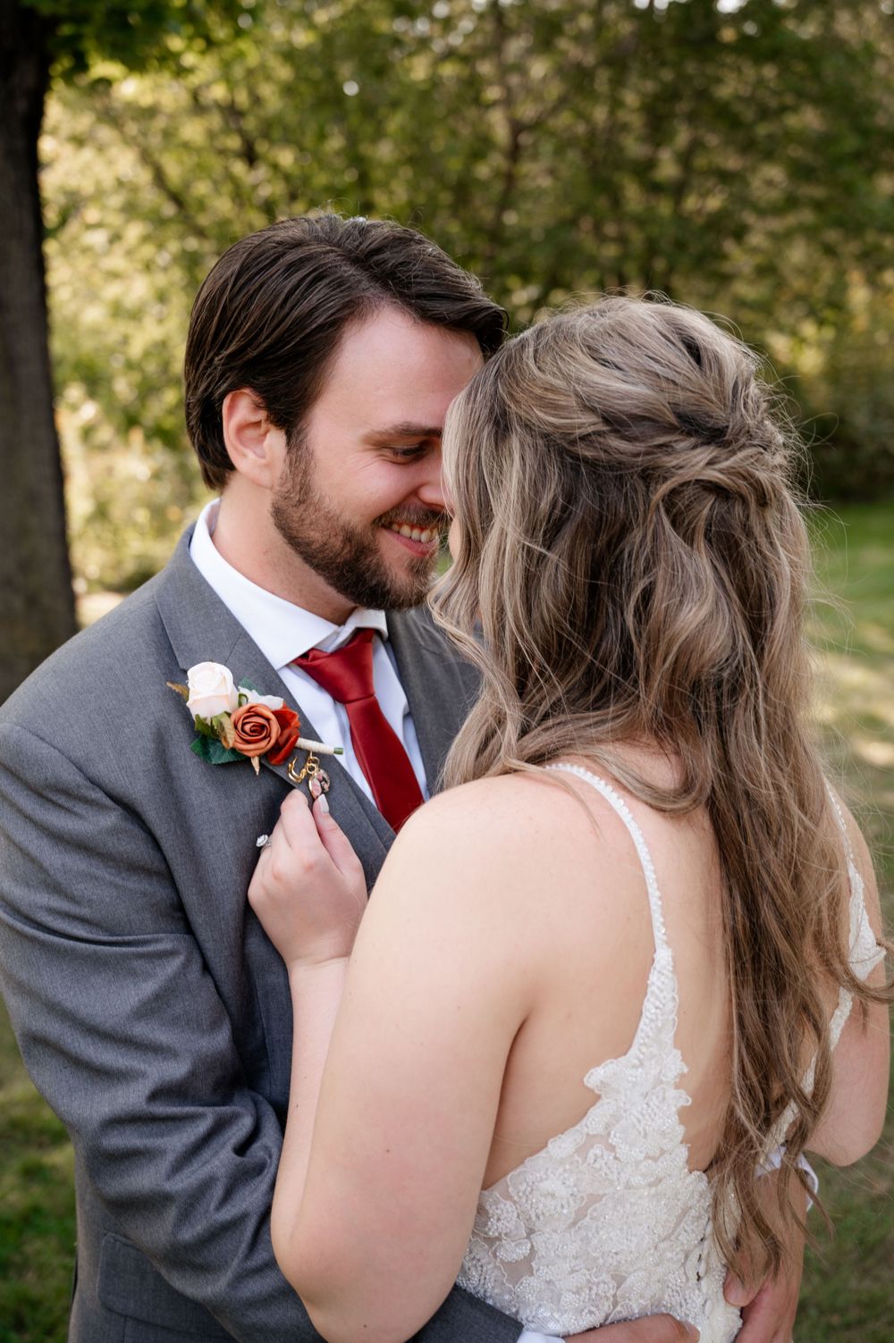 Smiling groom in gray suit with red tie and boutonniere sharing a tender moment with bride.