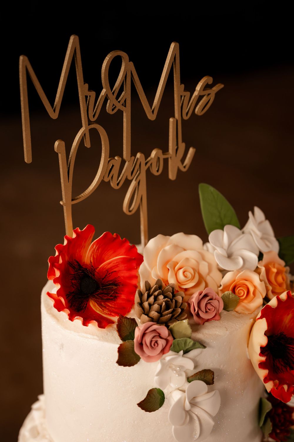 Close-up of Mr and Mrs Pagok wedding cake topper with red and blush sugar flowers.