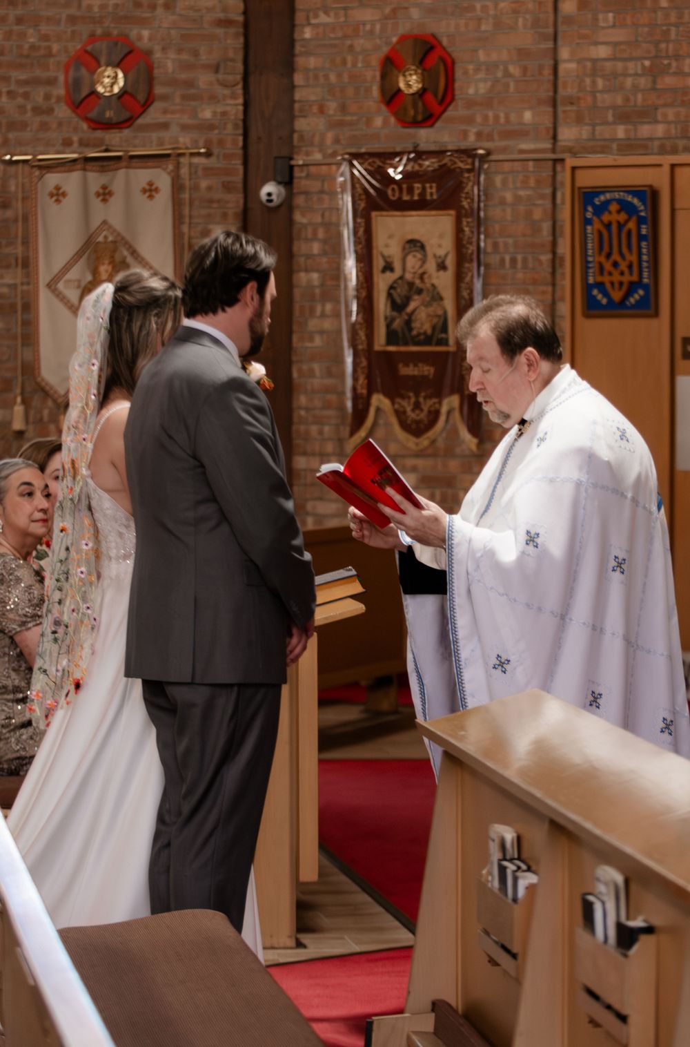 Bride and groom exchanging vows with priest in a Ukrainian Orthodox church ceremony.