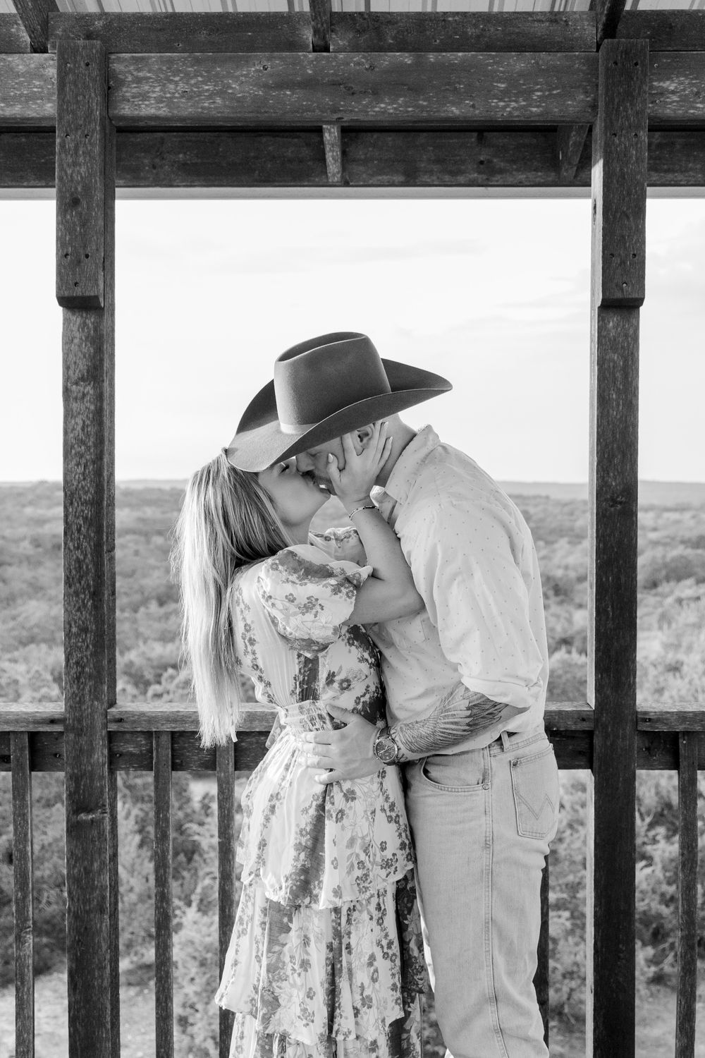 Black and White photo of Couple sharing a kiss after engagement at rustic arch in Dripping Springs, Texas Hill Country.