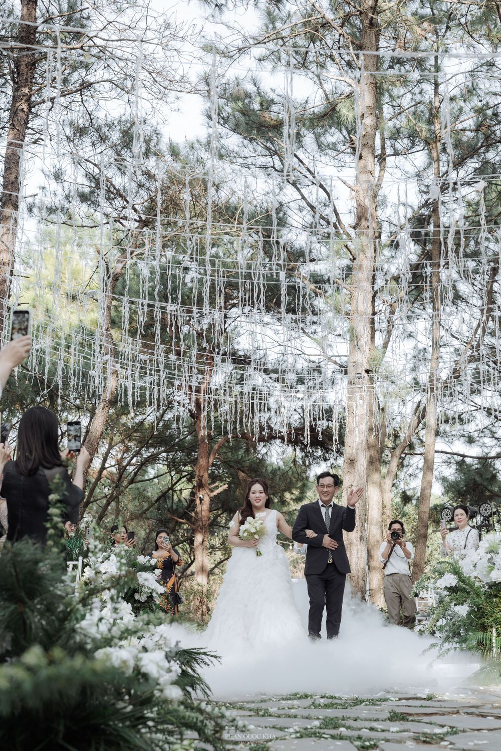 Bride and groom walk down the aisle at an enchanting outdoor forest wedding with hanging crystal decorations.