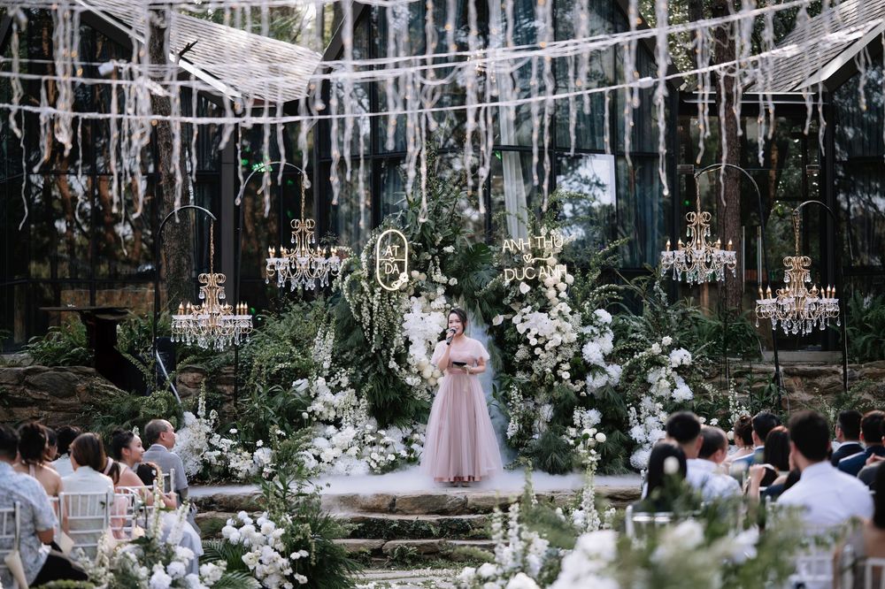 Elegant outdoor wedding ceremony in a forest venue with chandeliers, white florals, and seated guests.