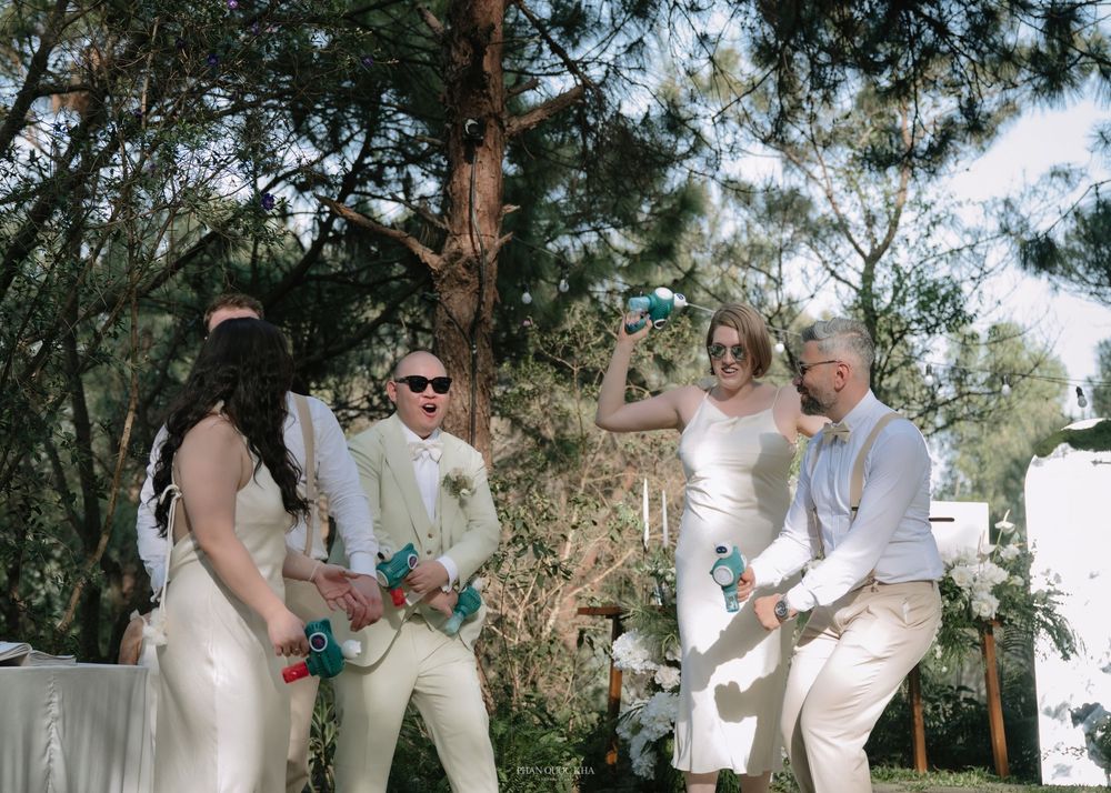 Wedding party celebrates outdoors with confetti poppers among pine trees in bright sunlight.