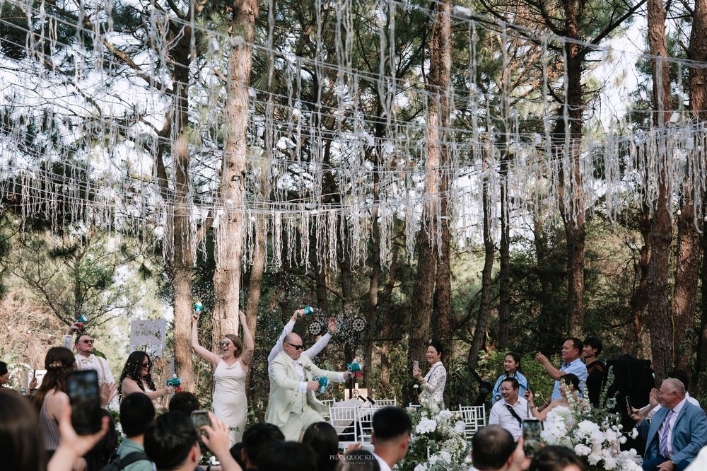 Bride and groom celebrate joyfully under a canopy of hanging crystals in a pine forest wedding ceremony.