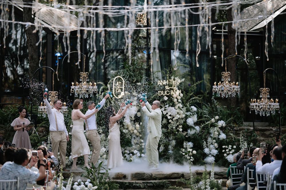Couple celebrating at a dreamy outdoor wedding with chandeliers, white florals, and confetti.