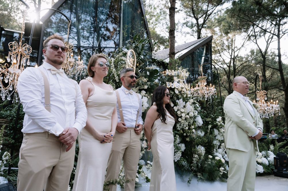 Wedding party in cream attire standing before a floral arch at an elegant outdoor ceremony.