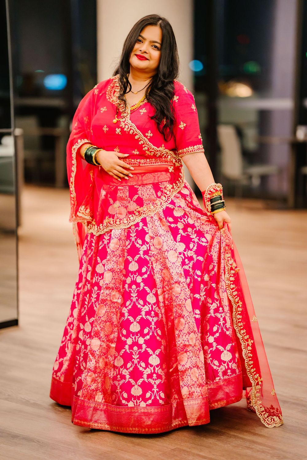 Beautiful traditional Indian bridal lehenga in bright pink and red with intricate gold embroidery on a wooden floor.