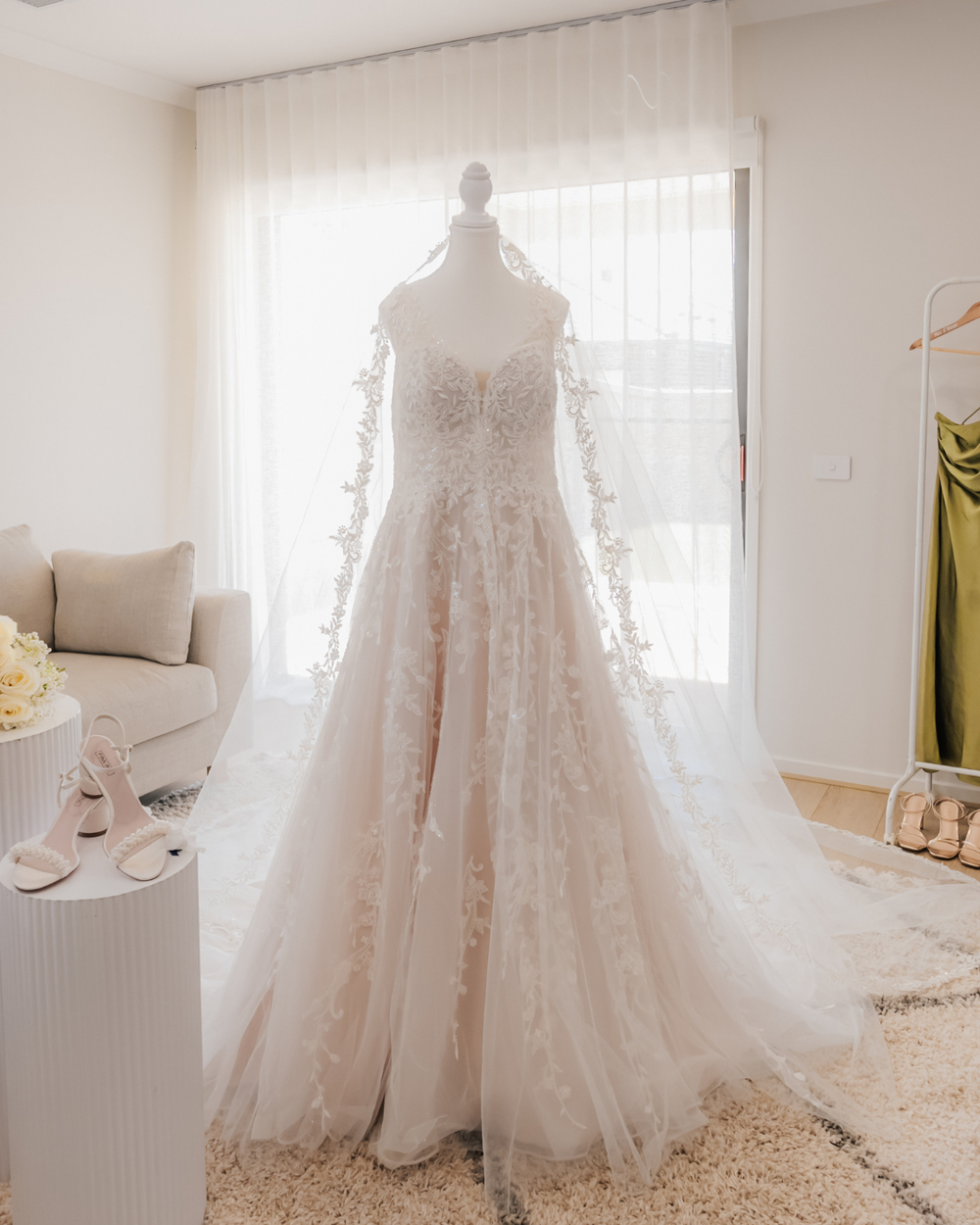 A romantic lace wedding dress with long sleeves and floral appliques displayed on a mannequin in a bright room.