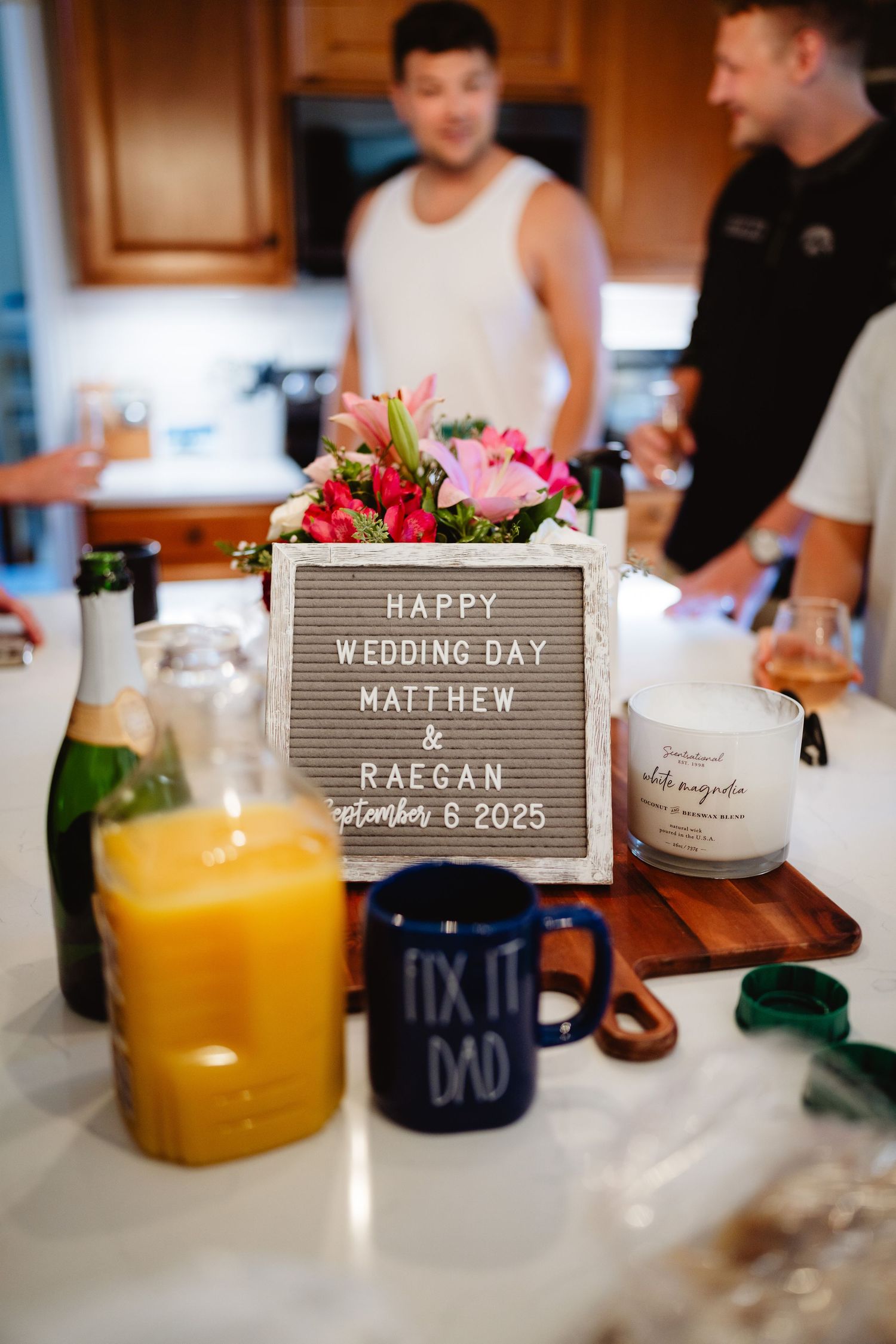 Small wooden signs and table settings with orange juice glasses display wedding day details and text.