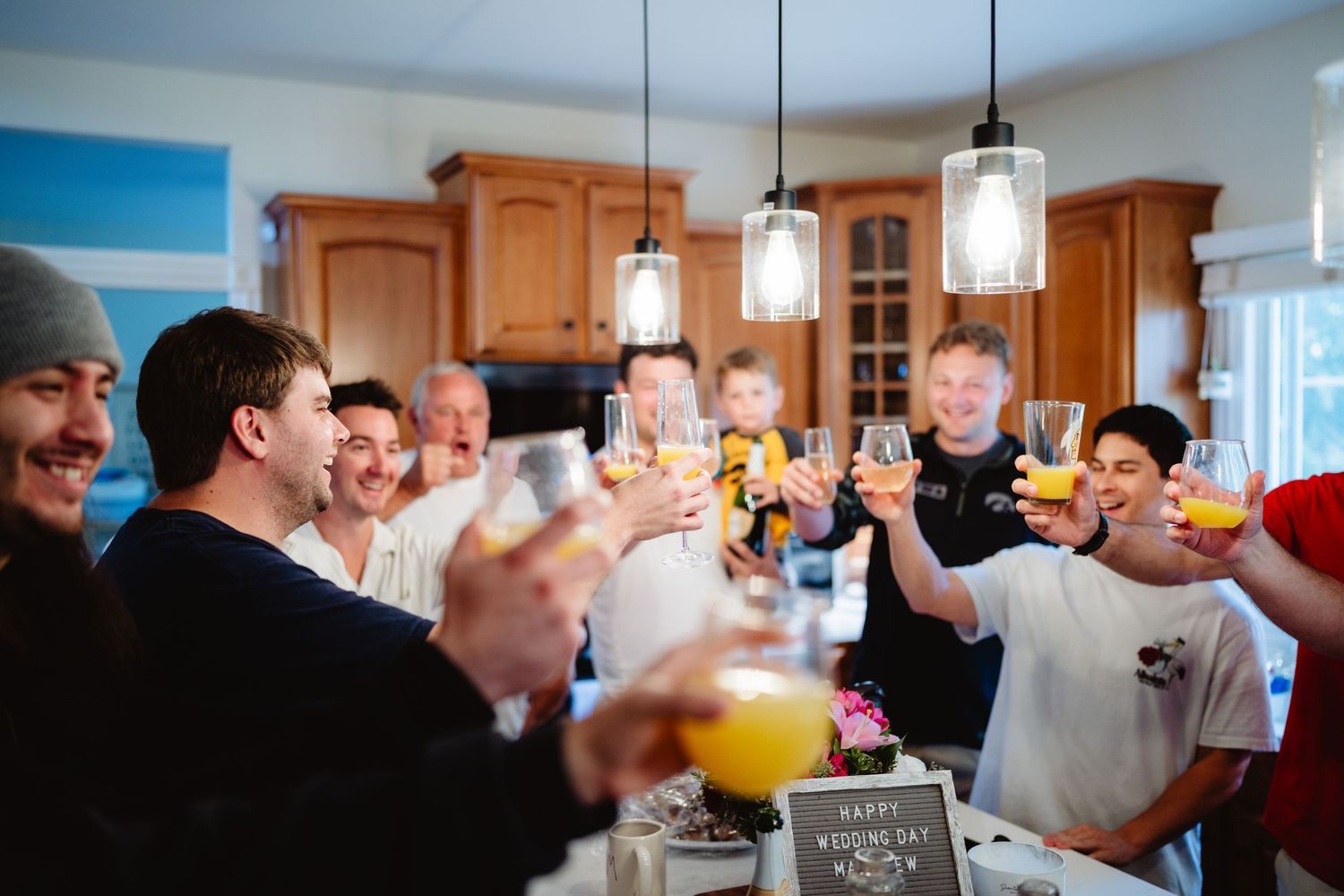 A group of people gather at a party to toast with drinks in a well-lit room.