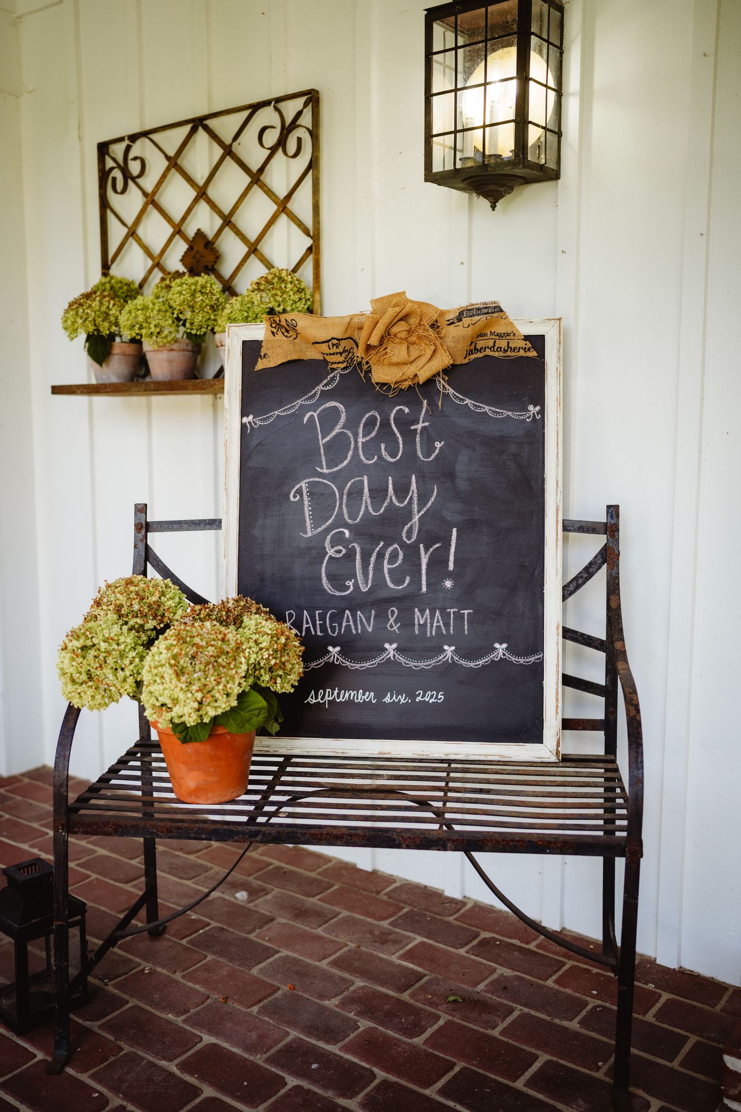 Rustic wooden benches with chalkboard signs and potted hydrangeas create a charming wedding decor display on a brick porch.