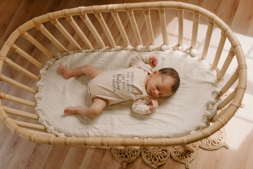 Sleeping infant lying in a curved wooden bassinet with white bedding.