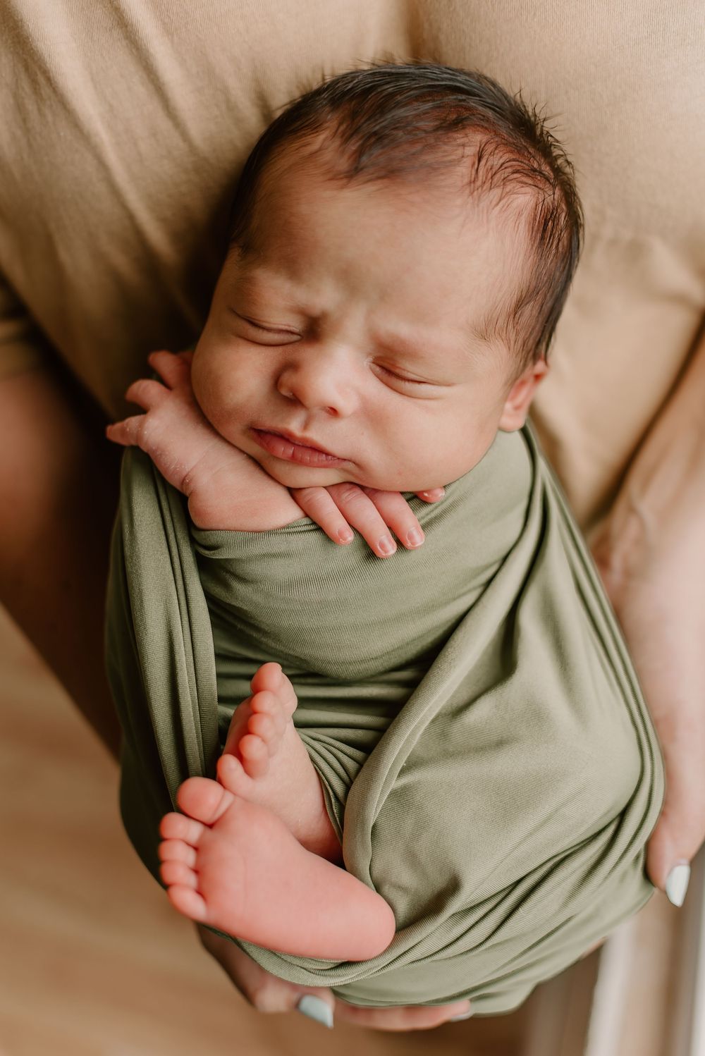 Sleeping newborn wrapped in sage green fabric showing tiny feet and peaceful expression.