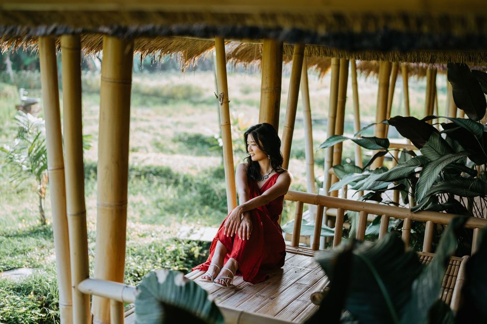 Elegant figure in red dress poses in bamboo pavilion surrounded by tropical foliage.