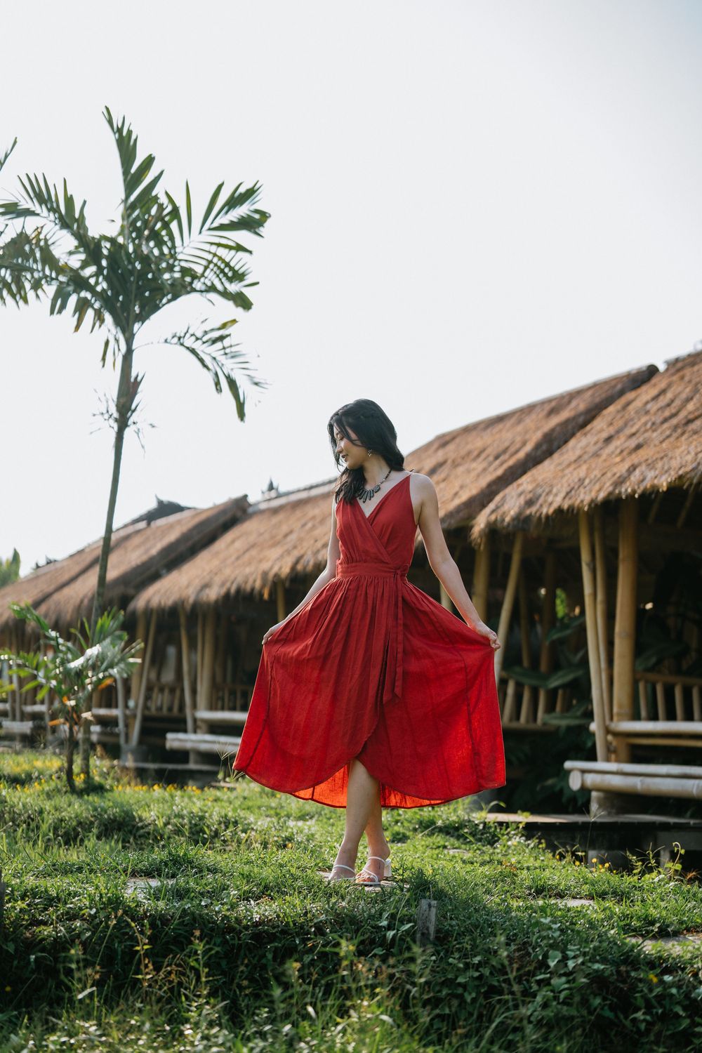 A flowing red dress twirls against tropical landscaping and traditional thatched roof bungalows.
