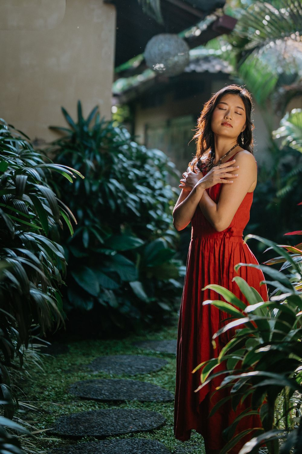 Elegant red dress creates striking contrast against tropical greenery in a garden setting.