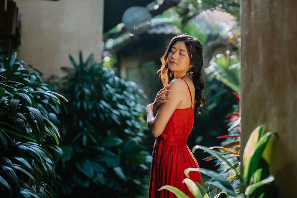 Dramatic lighting highlights a red dress among tropical foliage and garden shadows.