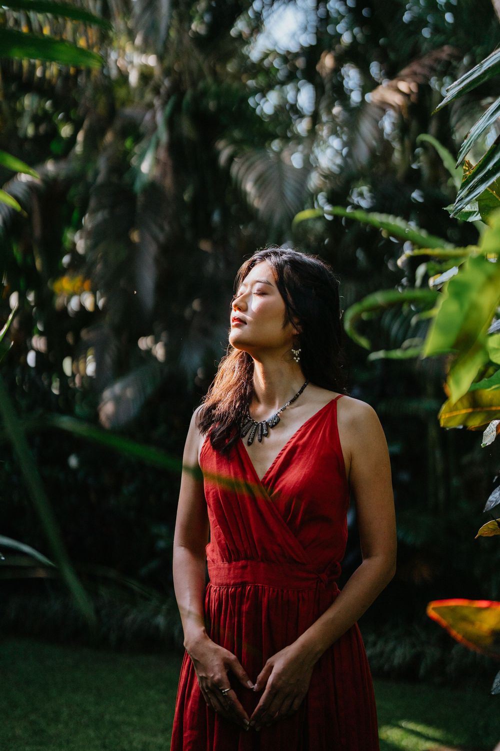 Sunlit garden scene featuring flowing red dress amid tropical greenery.