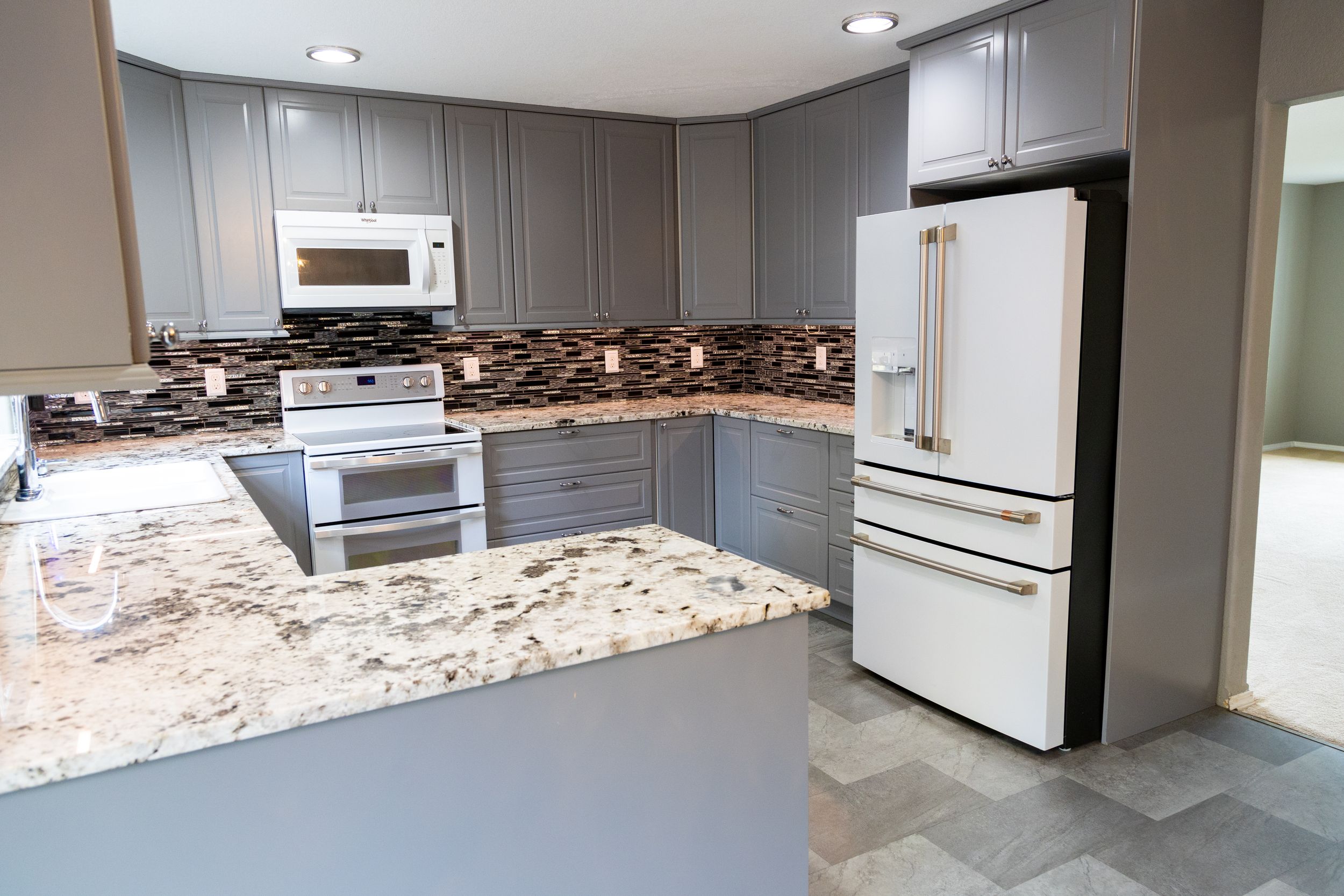 Modern kitchen with gray cabinets, granite countertops, and white appliances features a stylish mosaic tile backsplash.