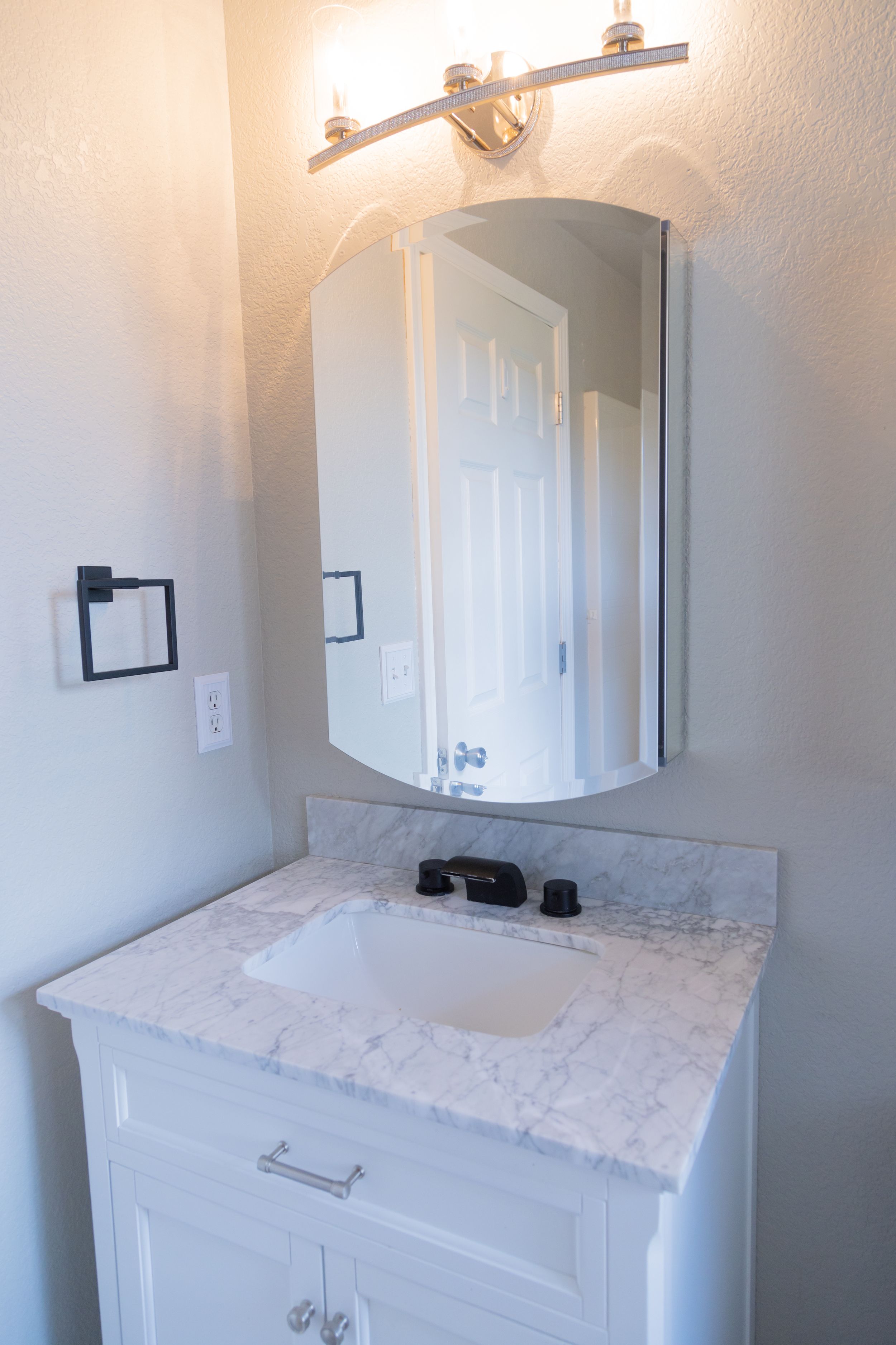 Bright bathroom vanity with white marble countertop, round mirror, and contemporary wall sconce lighting.