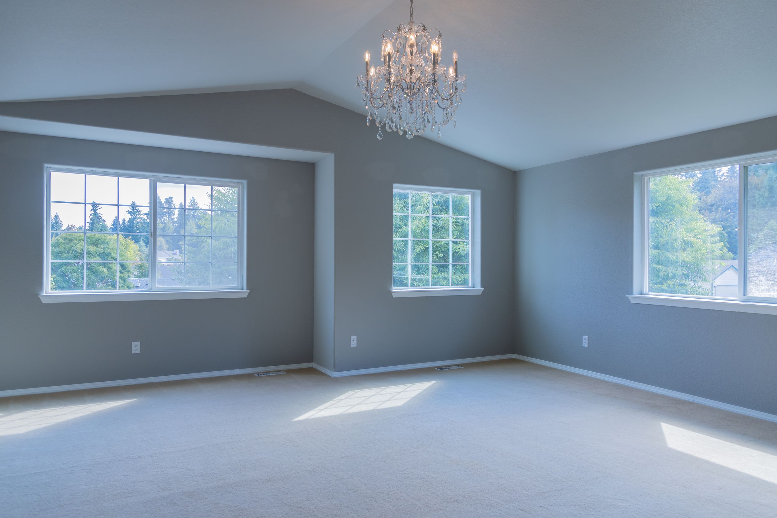 Large open room with blue-gray walls, chandelier, and multiple windows providing natural lighting.