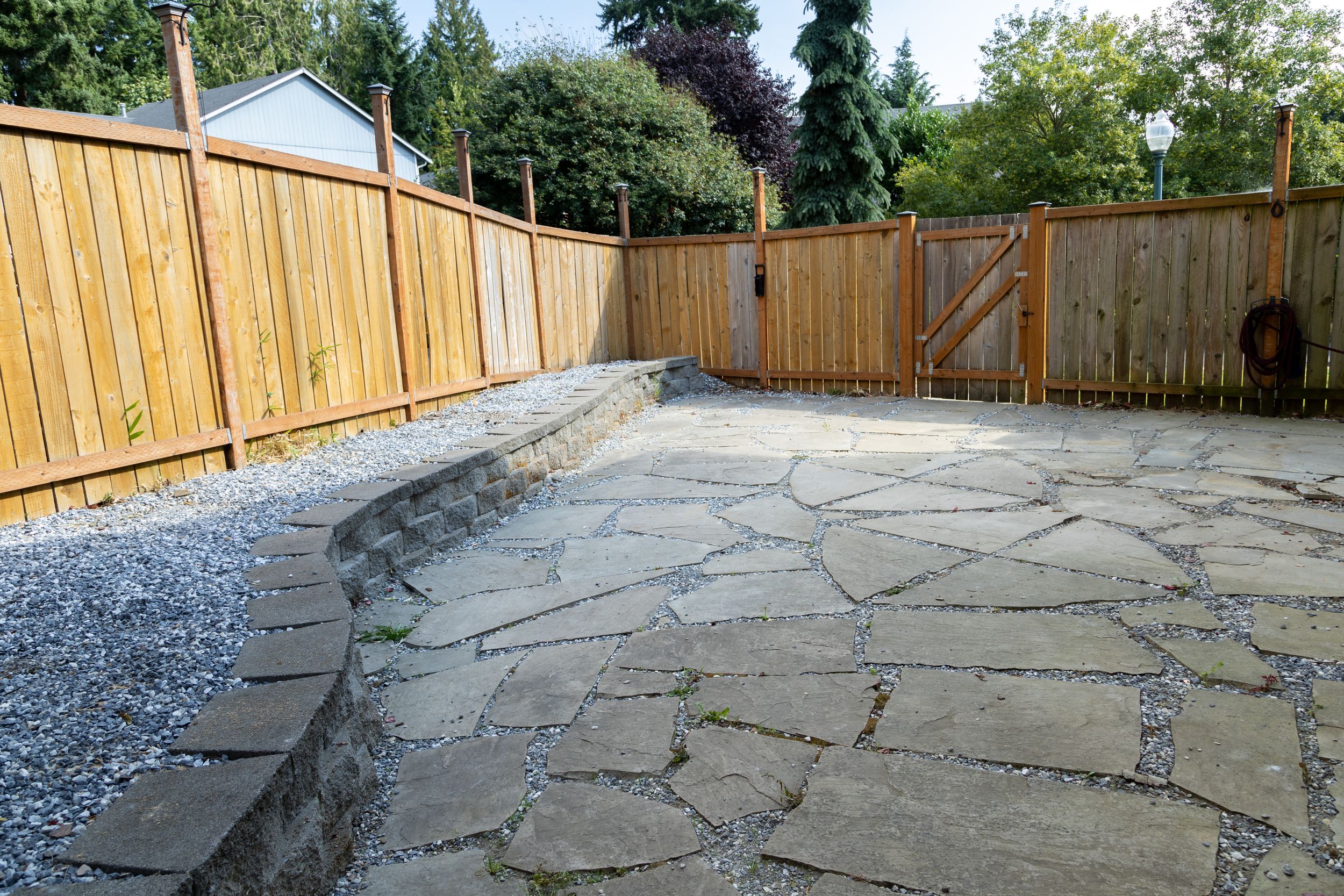 Stone path walkway curves through backyard with wooden privacy fence and gravel border along the edges.