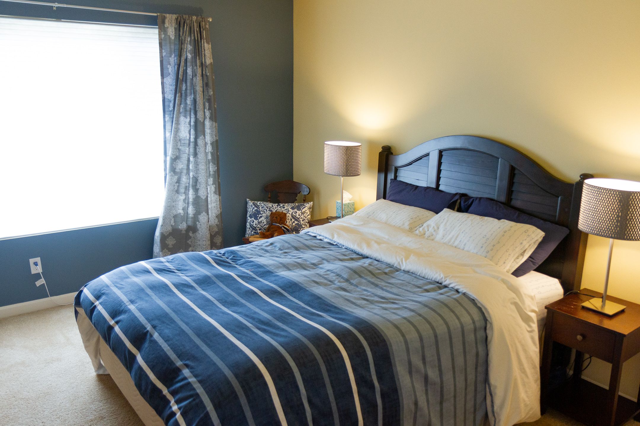 Modern bedroom with dark wood headboard, striped blue comforter, white sheets, and matching side table lamps.