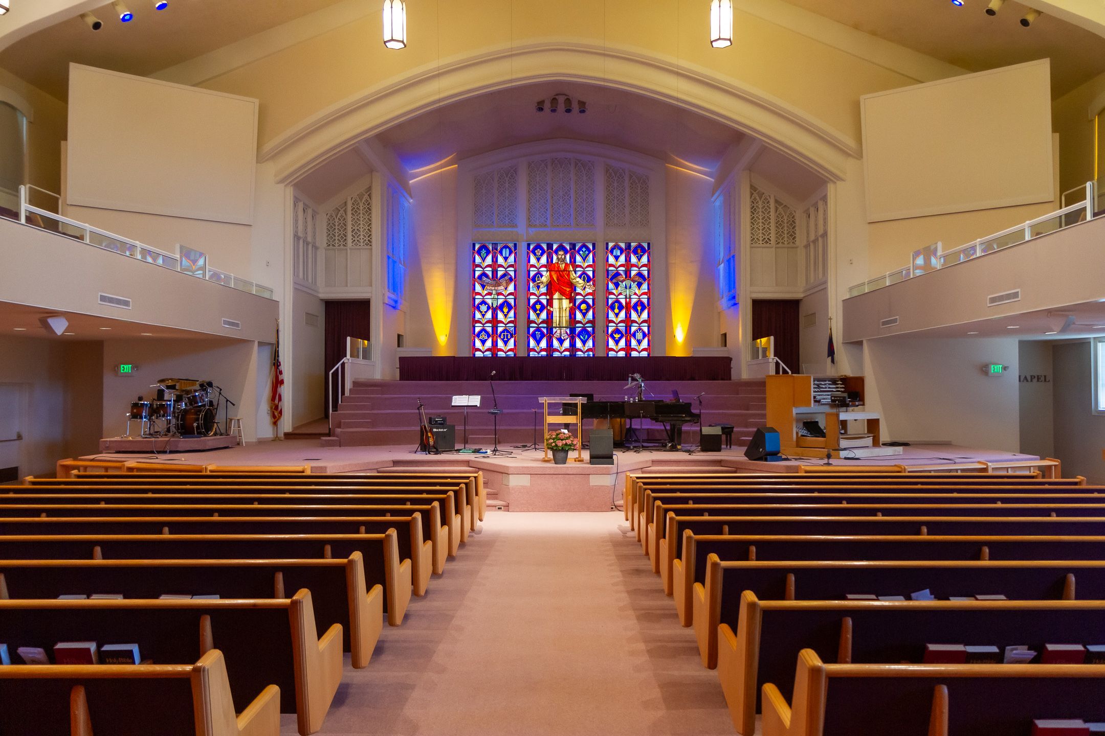 Interior view of an empty modern church sanctuary with wooden pews and stained glass windows illuminated by soft lighting.