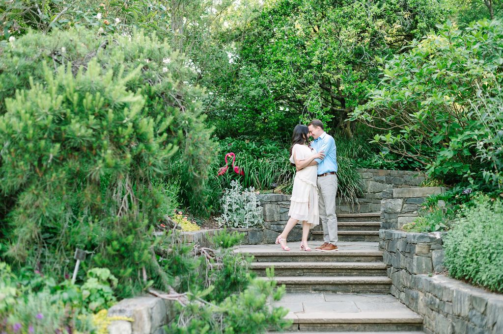 A couple walk hand in hand through a serene garden path with stone steps and lush greenery.