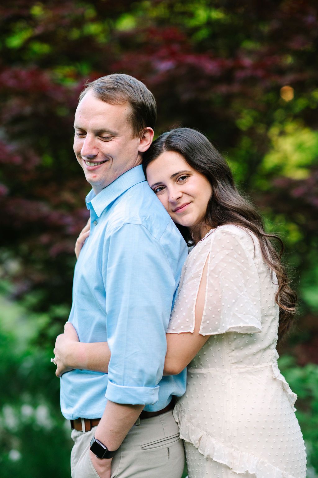A couple embraces outdoors in a natural setting with green foliage in the background.