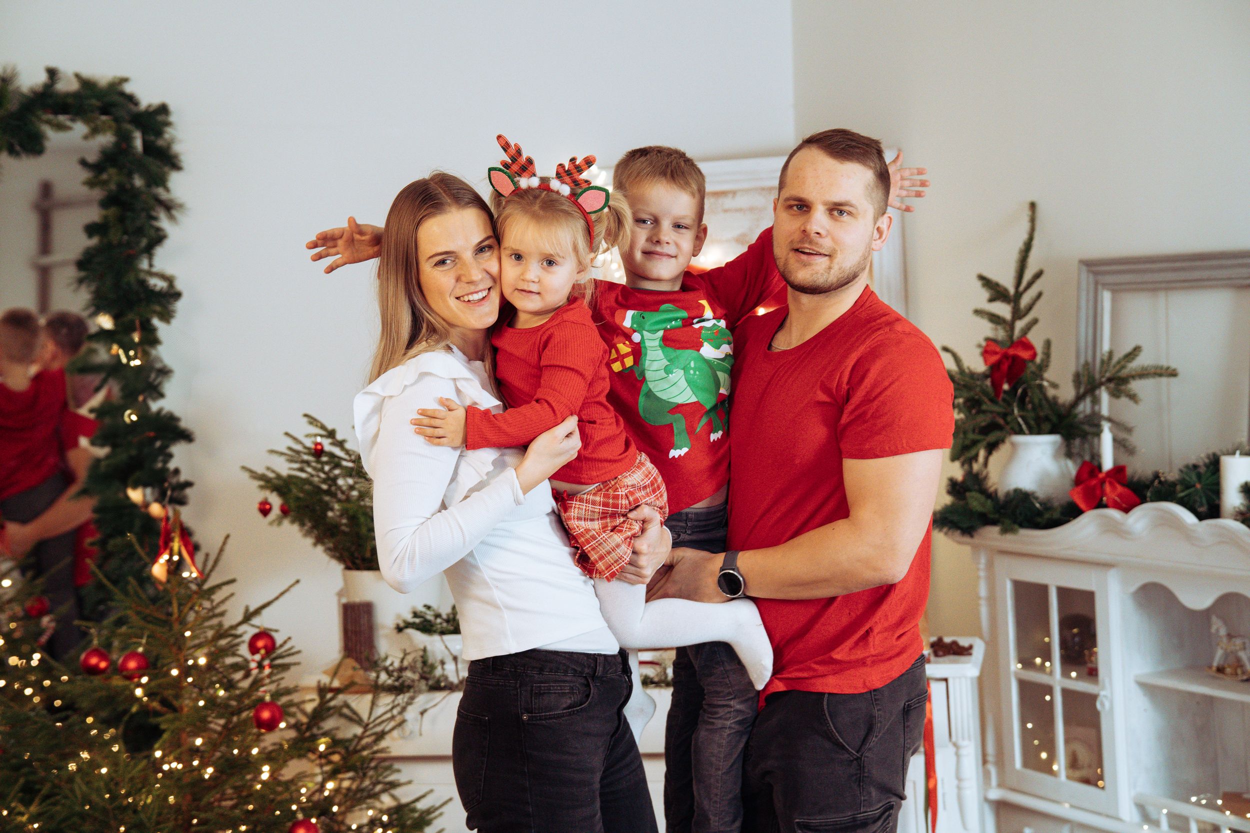 A family dressed in red and white poses together near a decorated Christmas tree for holiday photos.