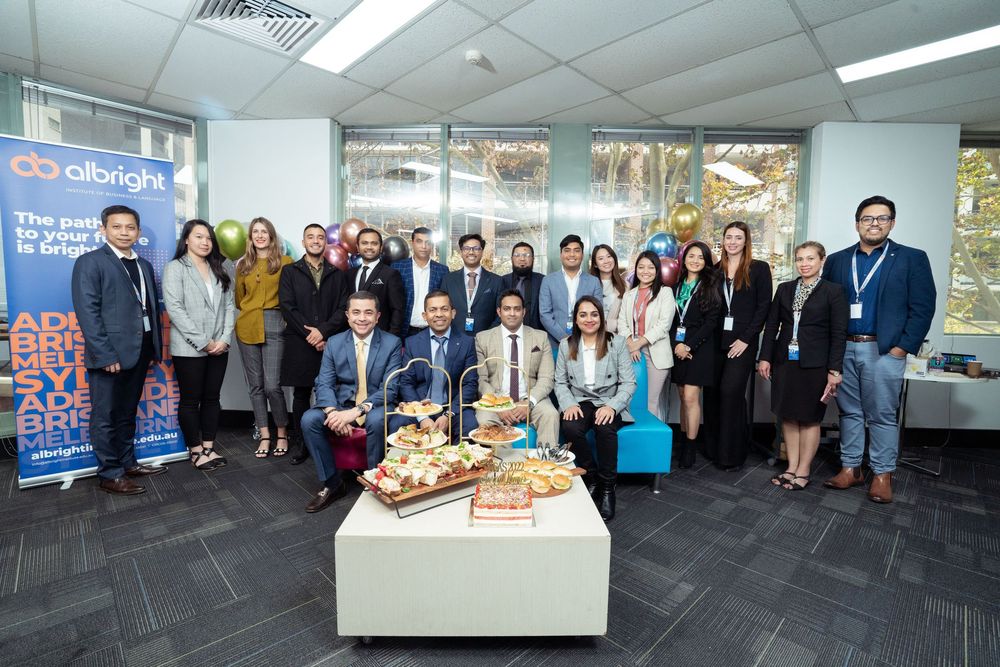 Corporate office event with team members gathered around displays and refreshments in a modern workspace.