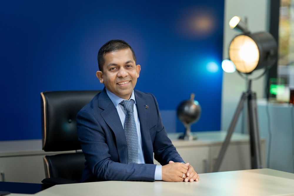 Professional headshots in a modern office setting with blue walls and window lighting.