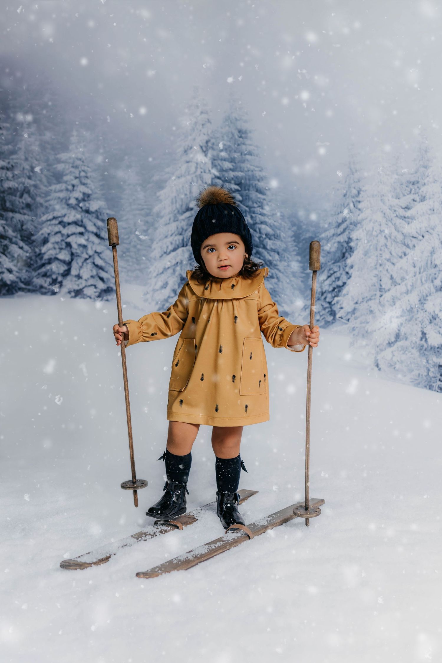Retrato de una niña disfrutando de una sesión de fotos navideña esquiando con abetos navideños de fondo.