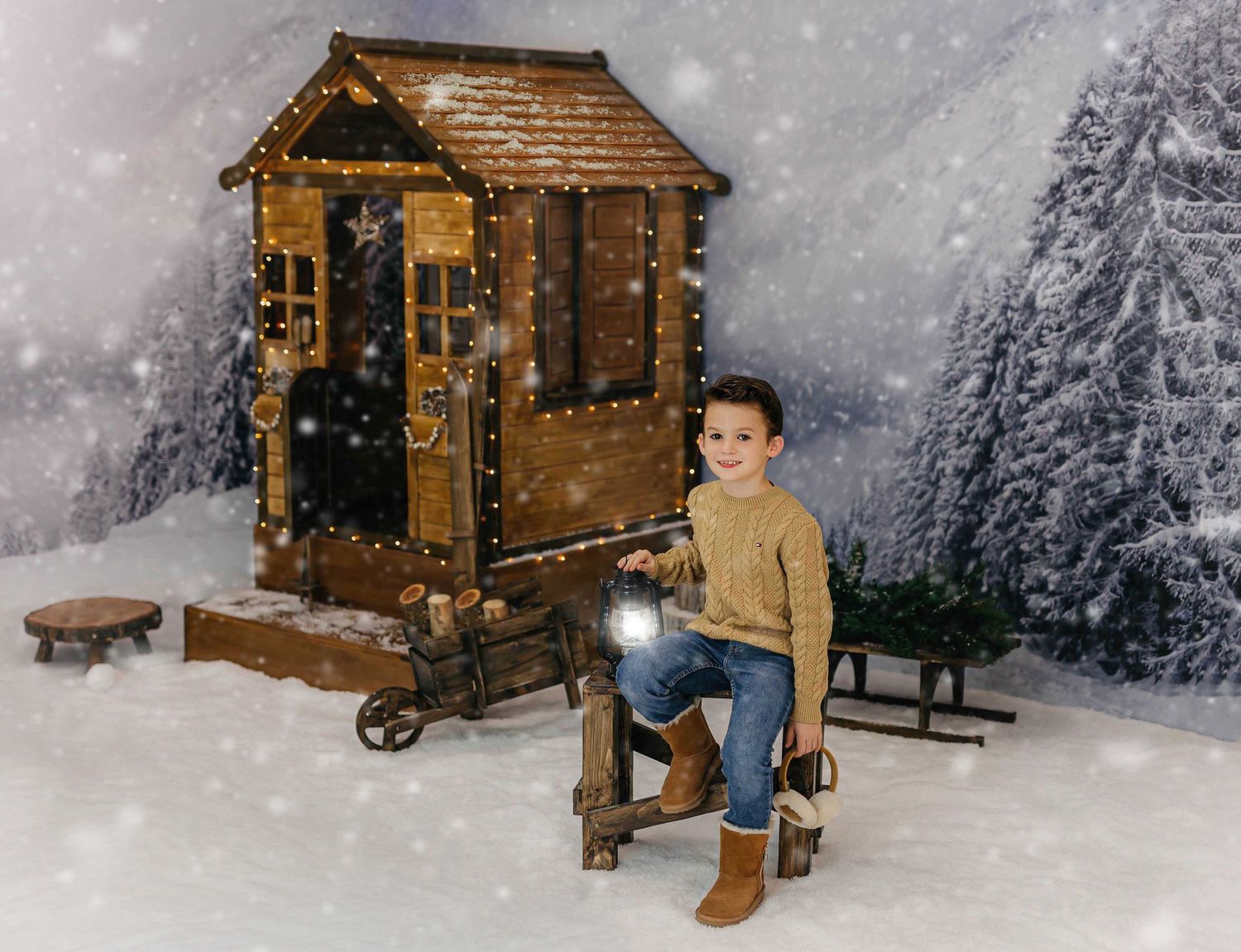 Retrato de un niño disfrutando de una sesión de fotos navideña sentado fuera de la casita navideña de fondo con nieve.