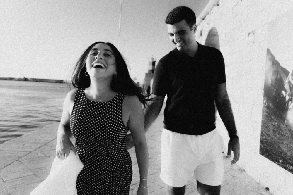 A couple laughing and running playfully along the beach in monopoli puglia at sunset.