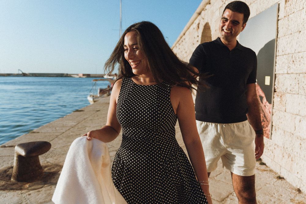 A group of five photos shows people walking and posing along a stone wall near the ocean during sunset.