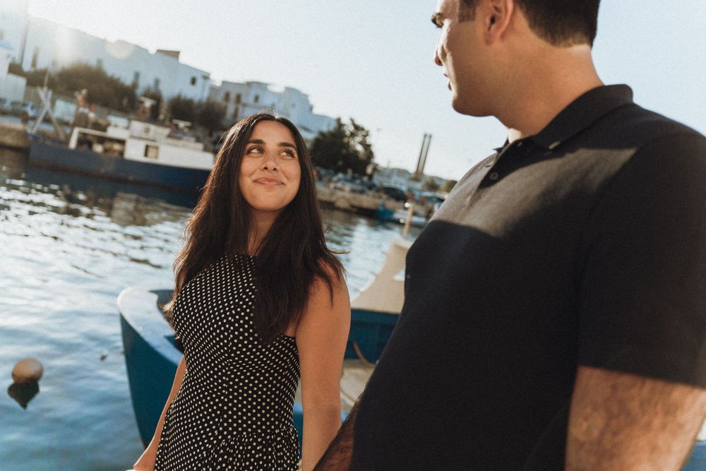 A couple sits together on a boat deck overlooking the water during golden hour in a coastal marina setting.