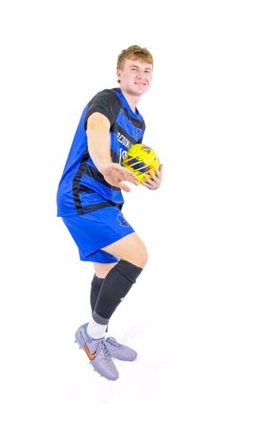 Soccer athlete in blue and black uniform jumping while holding yellow ball.