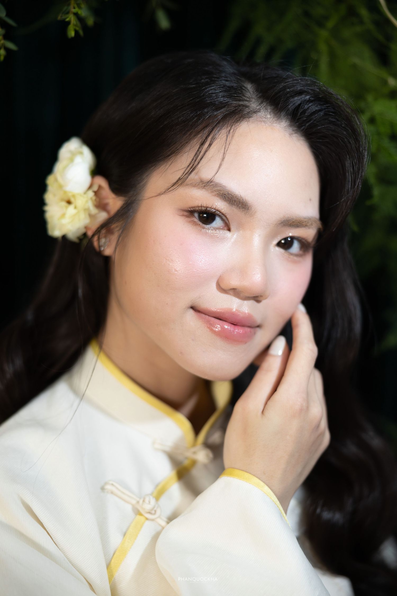 Beautiful young Asian woman in white ao dai with a yellow flower in her hair touching her face gently.