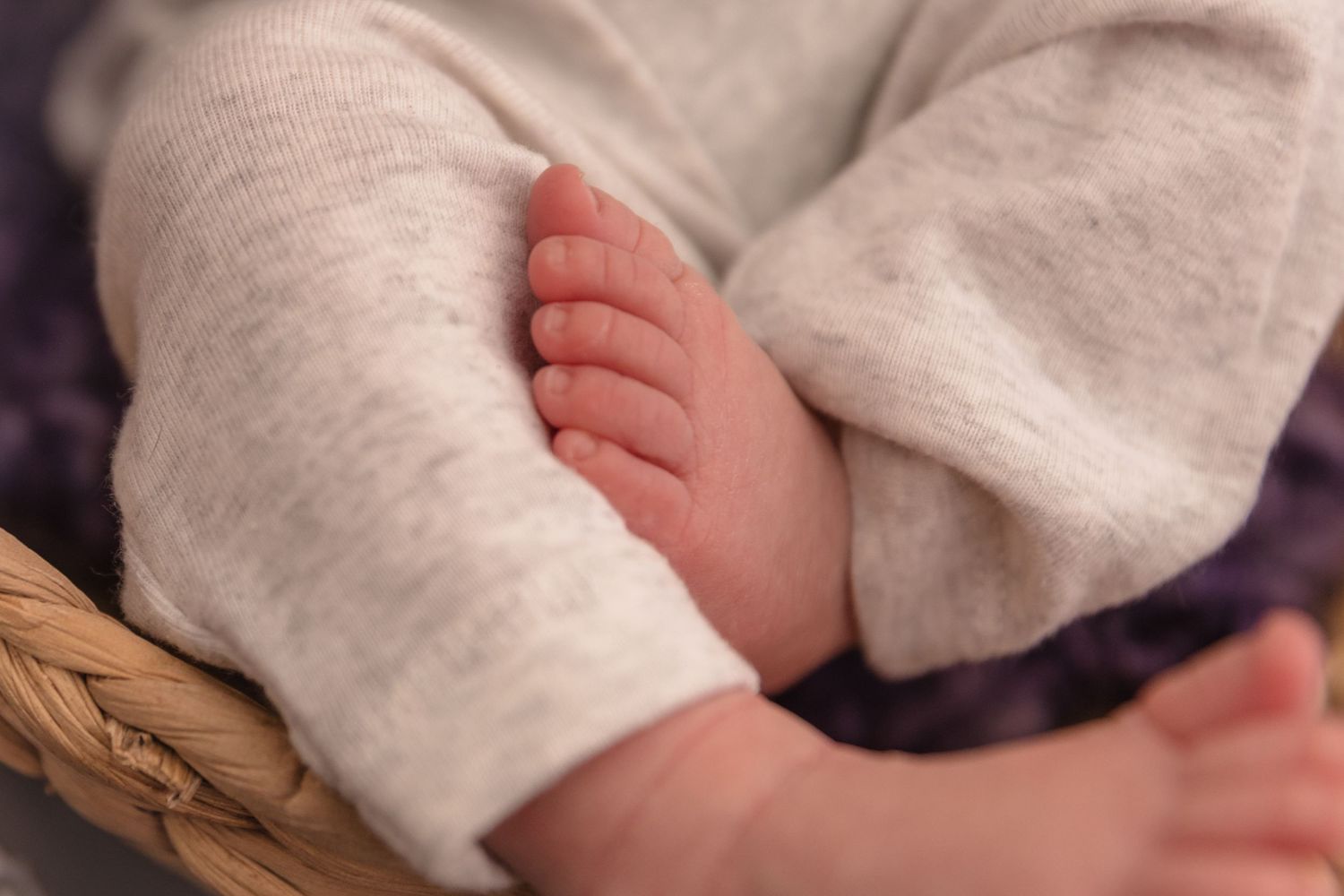 Close-up view of tiny baby feet wrapped in soft white blanket resting in woven basket.
