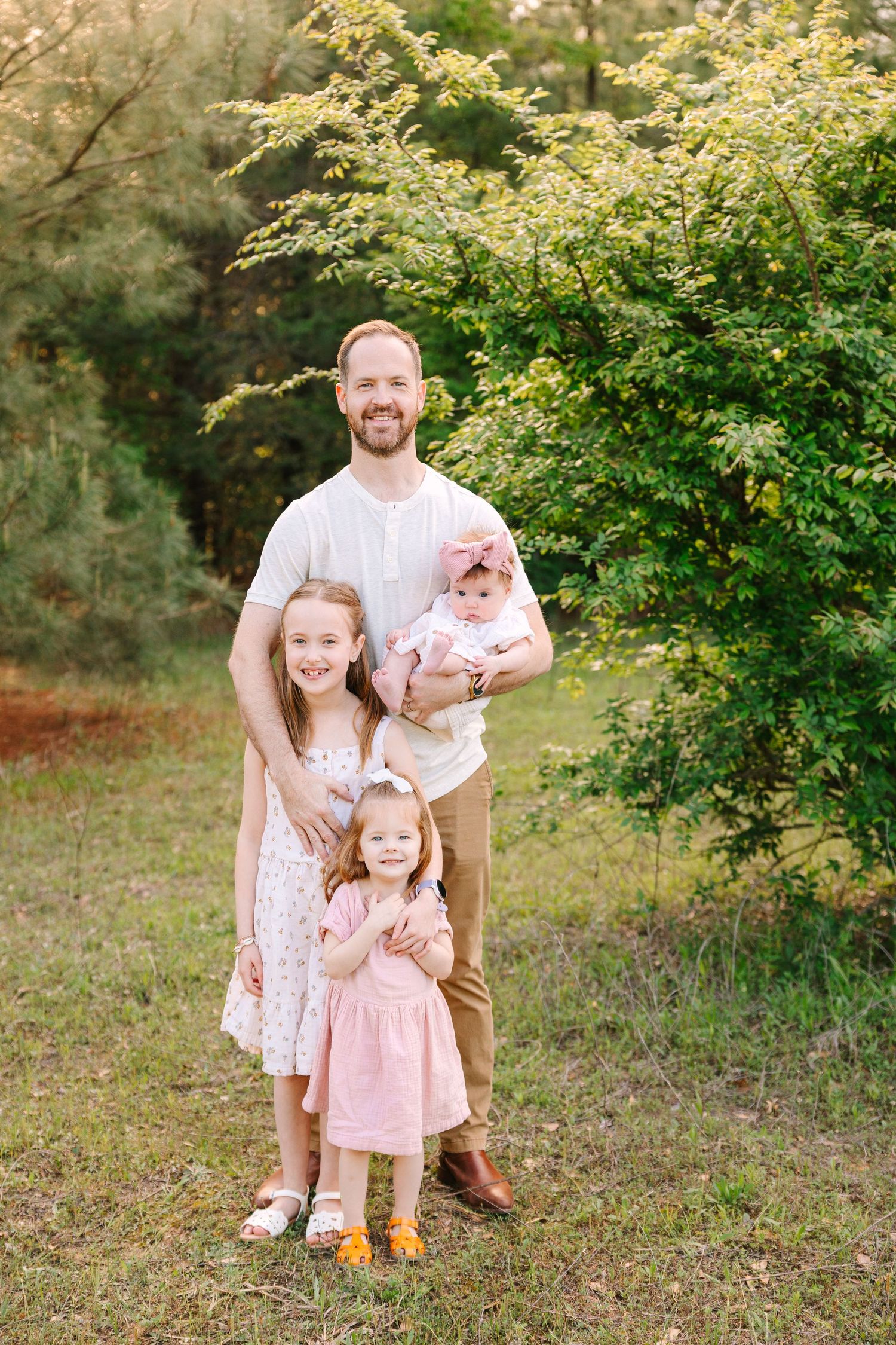 A family poses together for outdoor autumn portraits in a grassy area with leafy trees in the background.