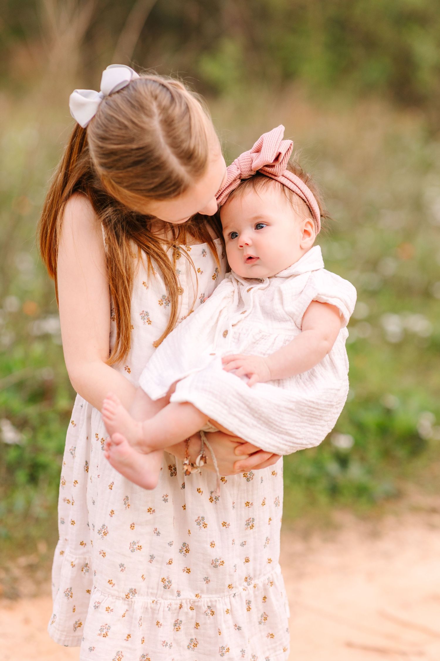A tender moment outdoors with a baby wearing a pink dress being held against a natural background.