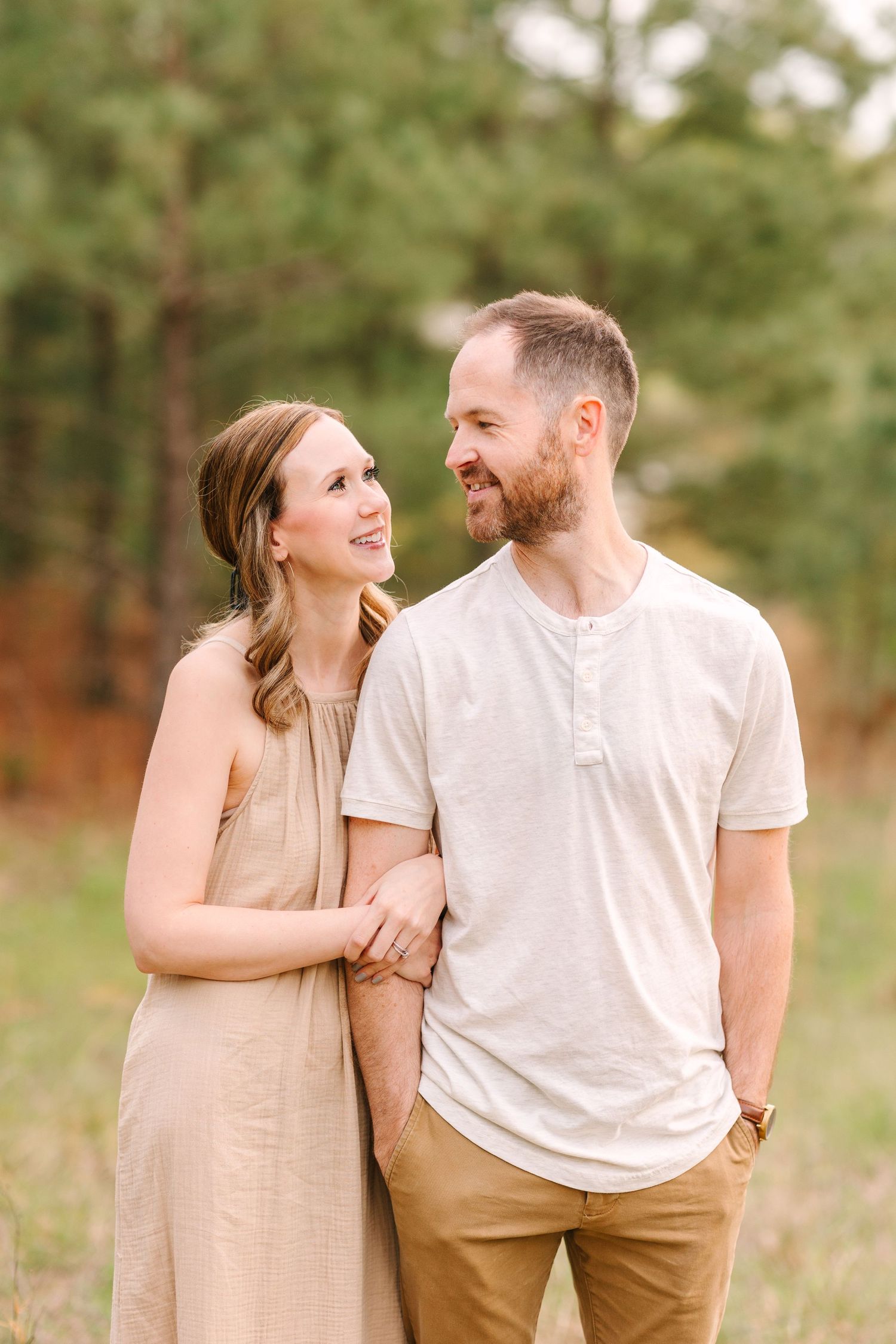 A couple shares intimate candid moments outdoors in coordinating neutral-toned outfits.
