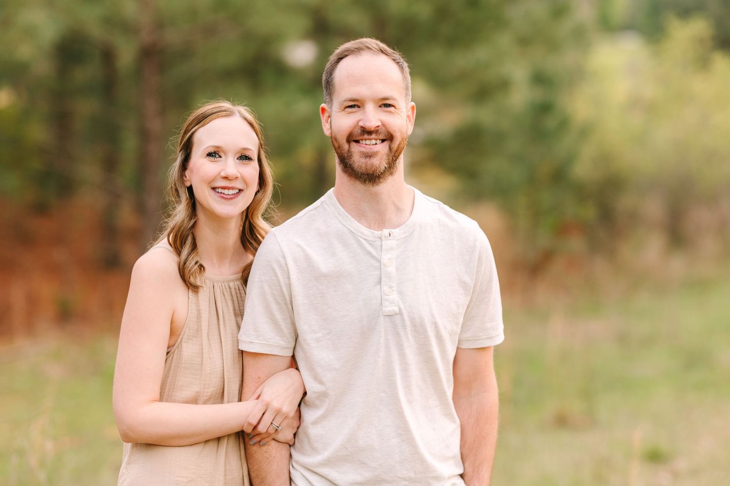 A smiling couple enjoys a tender moment together in an outdoor fall setting with warm natural lighting.