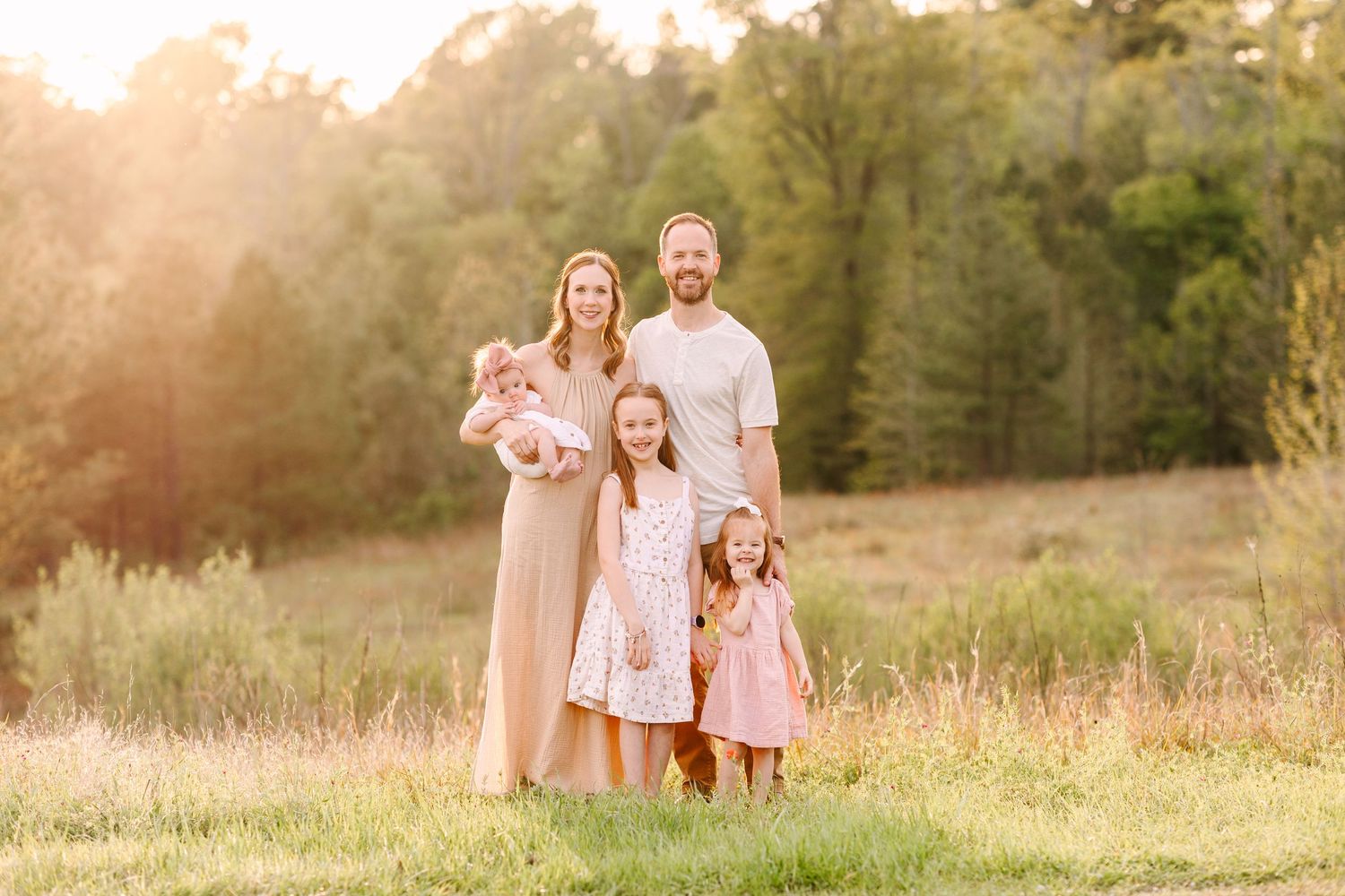 Sunlit outdoor photo session in a golden meadow during sunset with people in soft neutral and pink clothing.